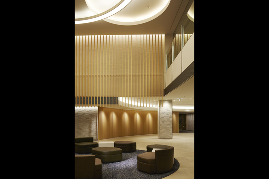 1階エントランスロビー　木目調ルーバーと間接照明、特注円形吊照明など各種の素材が寛ぎのロビー空間を演出する　©Forward Stroke inc.